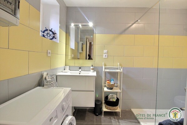A compact bathroom with a washing machine, a sink, and a shelf with toiletries.