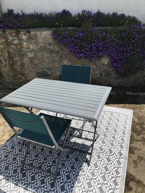 Relax on the patio with a table and chair, surrounded by a stone wall and lush greenery.