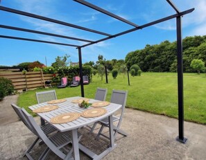 A covered patio with a table and chairs, surrounded by a grassy area and trees. - Sessile oaks - PLESLIN TRIGAVOU (PLESLIN TRIGAVOU)