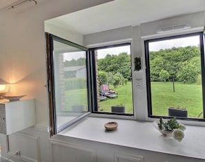 A room with a large window, a white desk, a bowl, and a potted plant.