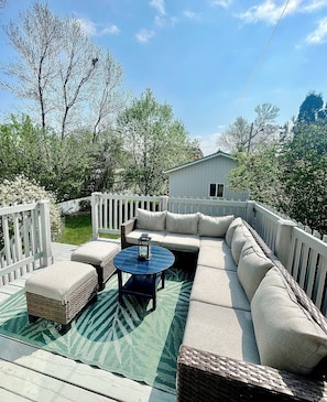 A deck with a sectional sofa, two ottomans, a round table, and a lantern.