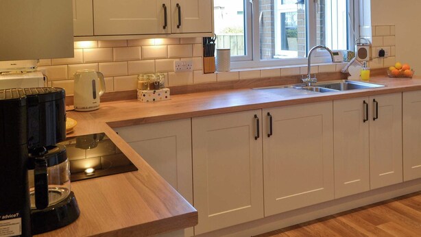 Een moderne keuken met witte kasten, een houten aanrecht, een koffieapparaat, een waterkoker en een raam met uitzicht.