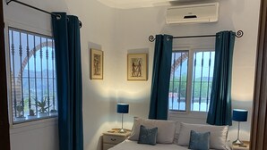 Ein Schlafzimmer mit Bett, Nachttischen, Deckenventilator und einem Fenster mit Vorhängen.