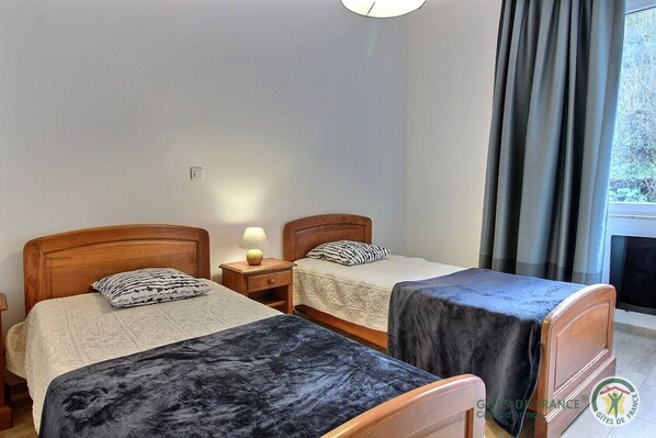 A room with two wooden beds, each with a pillow and a bedside table with a lamp.
