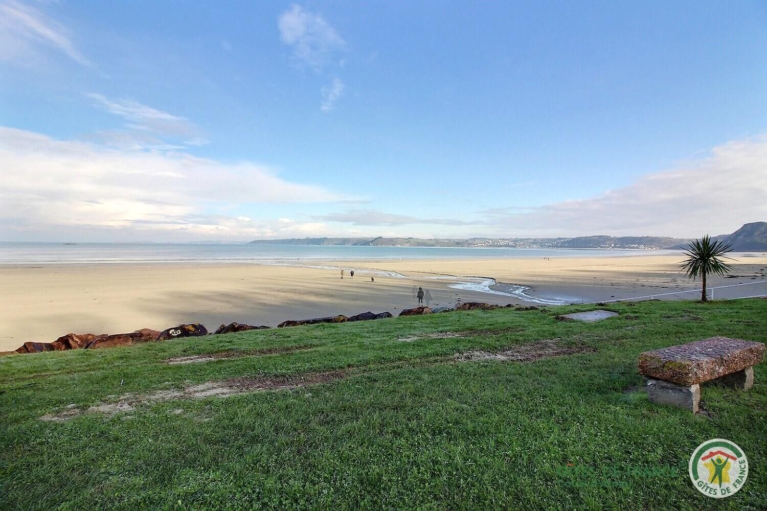 A coastal landscape with a sandy beach, grassy foreground, and a clear sky.
