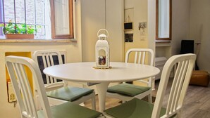Une table ronde blanche, entourée de quatre chaises blanches, chacune agrémentée d’un coussin vert. Une lanterne blanche, ornée d’un motif décoratif, est posée sur la table.