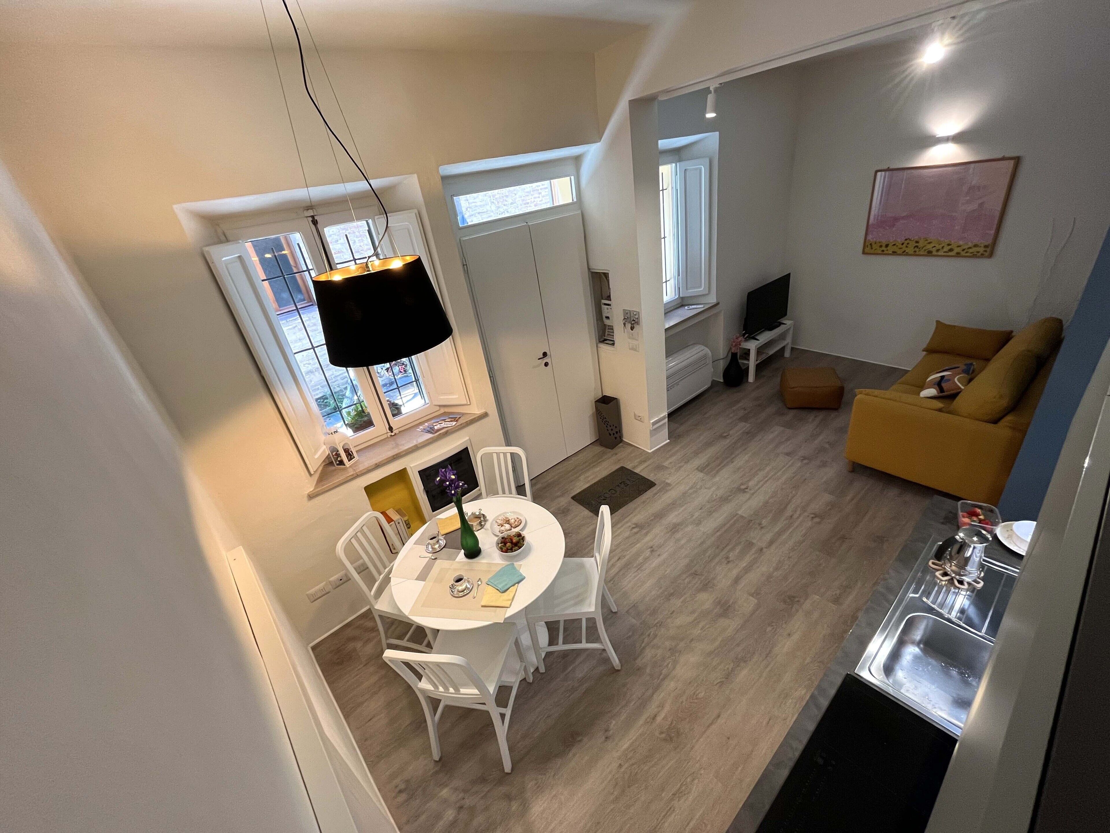 Een moderne keuken met een inbouwoven, een eethoek met een ronde tafel en witte stoelen, een bank en een televisie in de woonkamer.