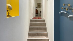 Un escalier avec des éléments en bois, bordé de murs peints en jaune et en bleu, mène à une pièce dont la porte est ornée de poignées métalliques.