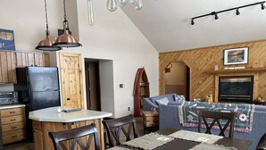 Uma cozinha compacta com geladeira, armários de madeira e um espaço de jantar com mesa posta para quatro pessoas.