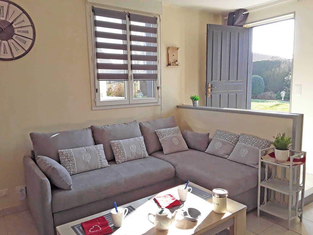 A living room with a grey sofa, a coffee table, a clock, and a window with blinds.