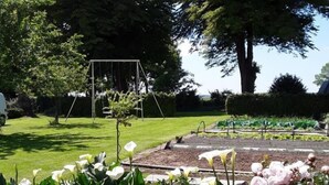 A garden with a swing set, flowering plants, and a large tree. - Gîtes de France® - Les Hirondelles (ST REMY BOSCROCOURT)