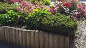 A house with a tiled roof, a garden with various plants and flowers, and a wooden fence. - Gîtes de France® - Les Hirondelles (ST REMY BOSCROCOURT)