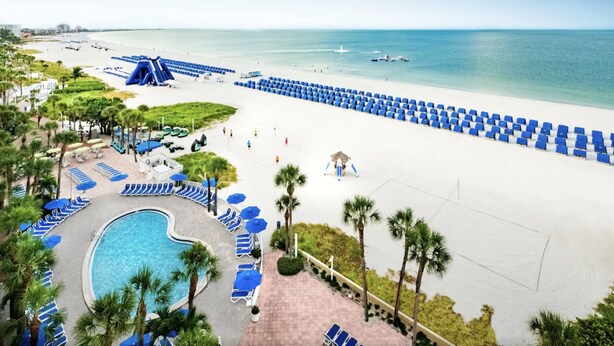 Un resort con piscina, spiaggia e lettini.