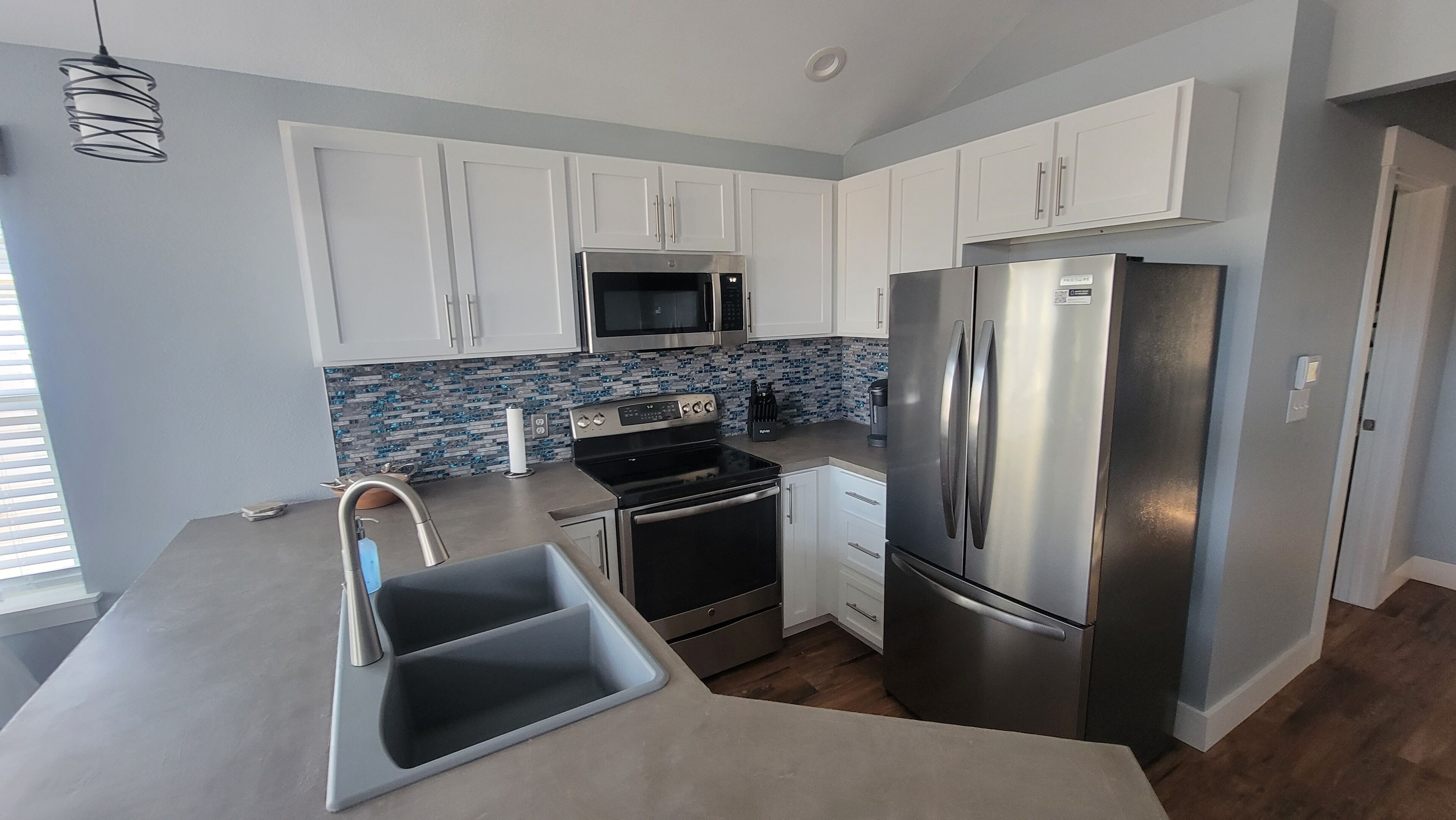 A modern kitchen with white cabinets, stainless steel appliances, and a blue-tiled backsplash.