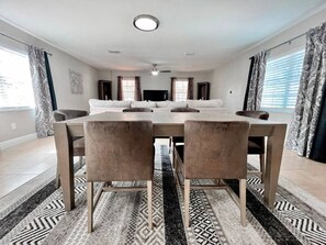 Comedor con una mesa larga y sillas, ventilador de techo y televisor.
