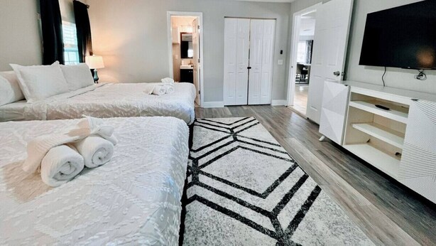 A hotel room with two beds, a ceiling fan, a TV, and a hallway leading to a bathroom.