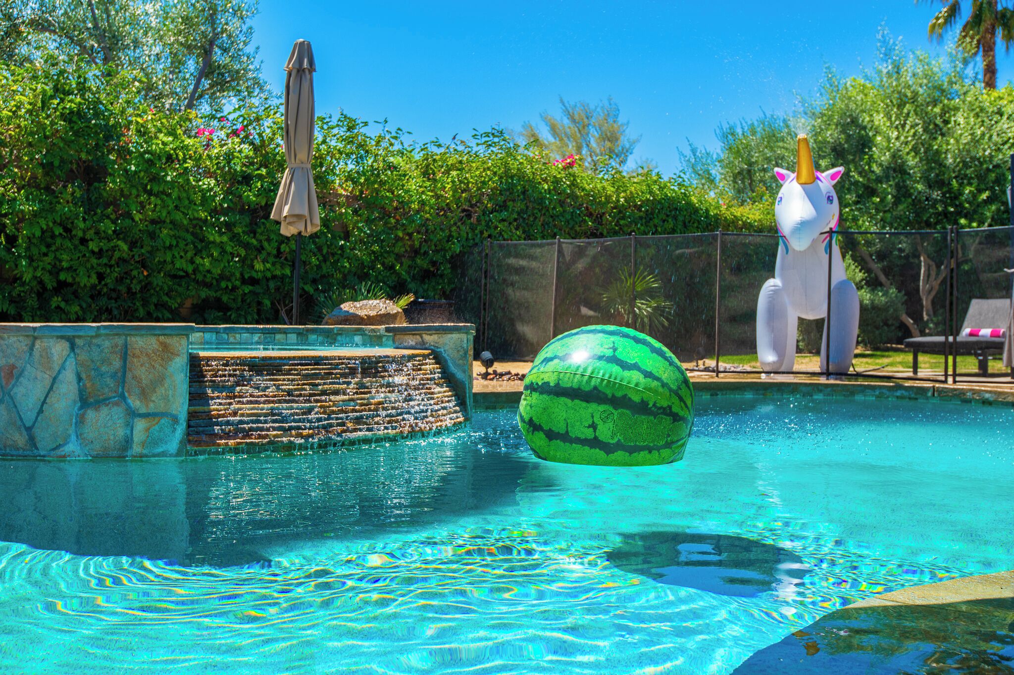 Uma piscina com escorrega, uma melancia inflável grande e uma decoração de unicórnio.
