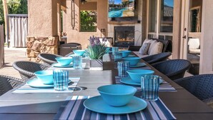 An outdoor dining area with a long table set with blue bowls and glasses, surrounded by wicker chairs. - Casa Serenity Luxury Living w/ Pool & Jacuzzi (Indio)