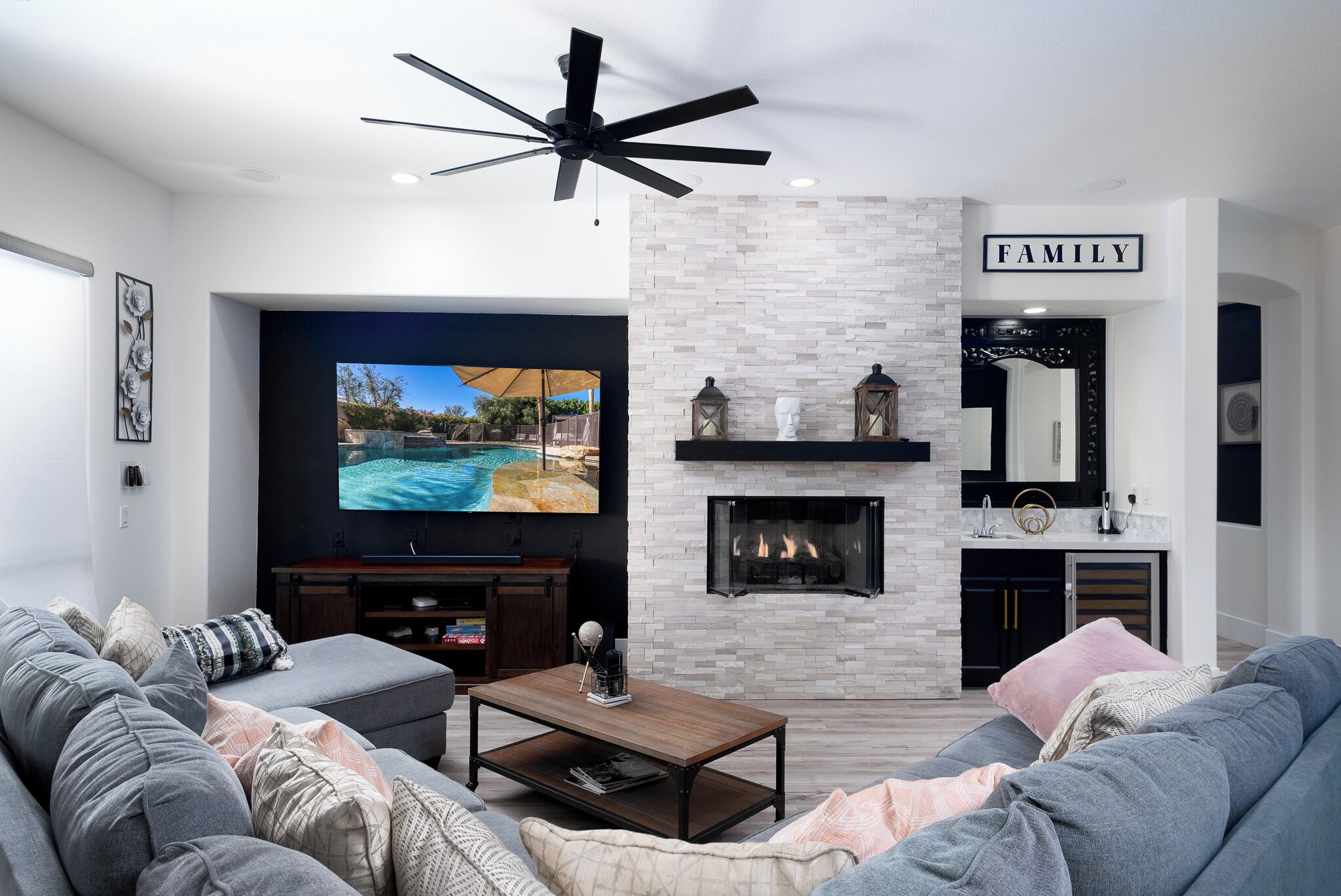 Een moderne woonkamer met een open haard, een plafondventilator en een aan de muur bevestigde televisie.