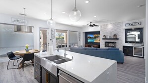 A modern kitchen with a central island, a dining area with chairs, a sofa, and a fireplace. - Casa Serenity Luxury Living w/ Pool & Jacuzzi (Indio)