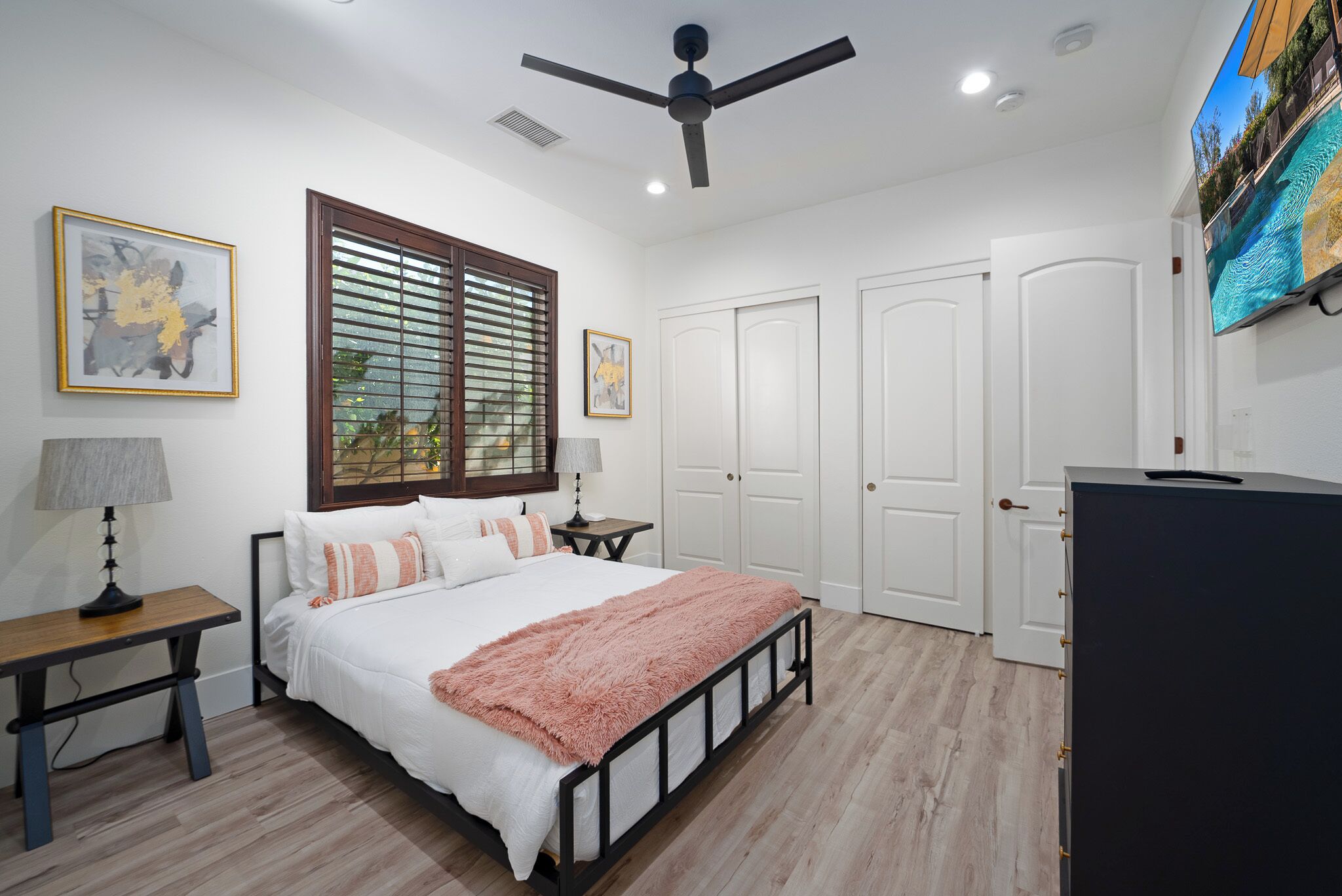 A bedroom with a bed, a ceiling fan, a TV, and a window with blinds.