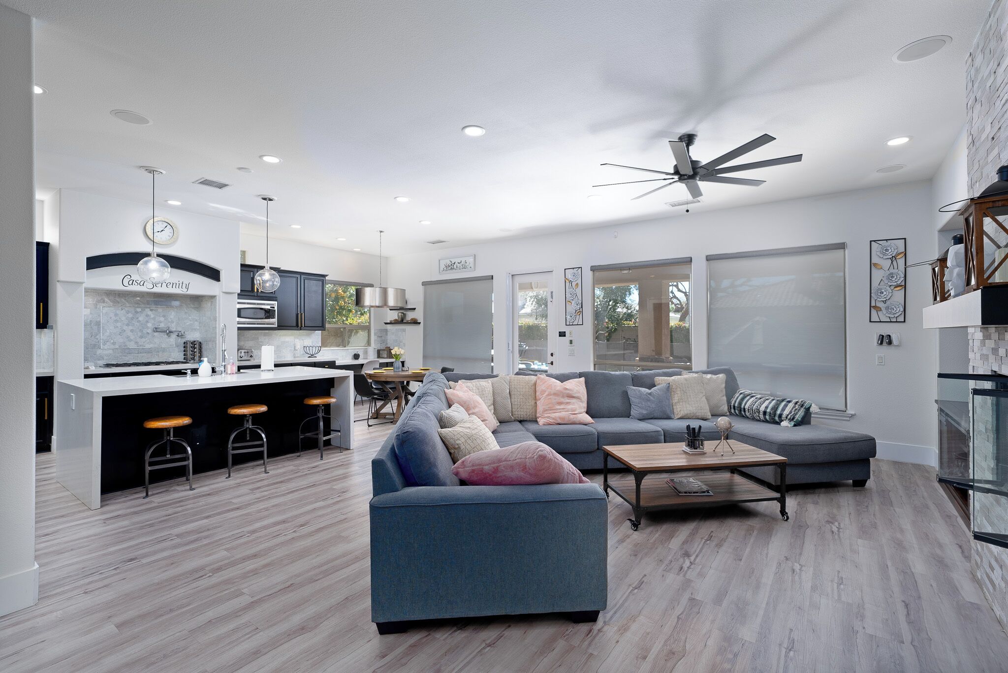 A modern living room with a grey sofa, a coffee table, and a kitchen area with a bar counter and stools.