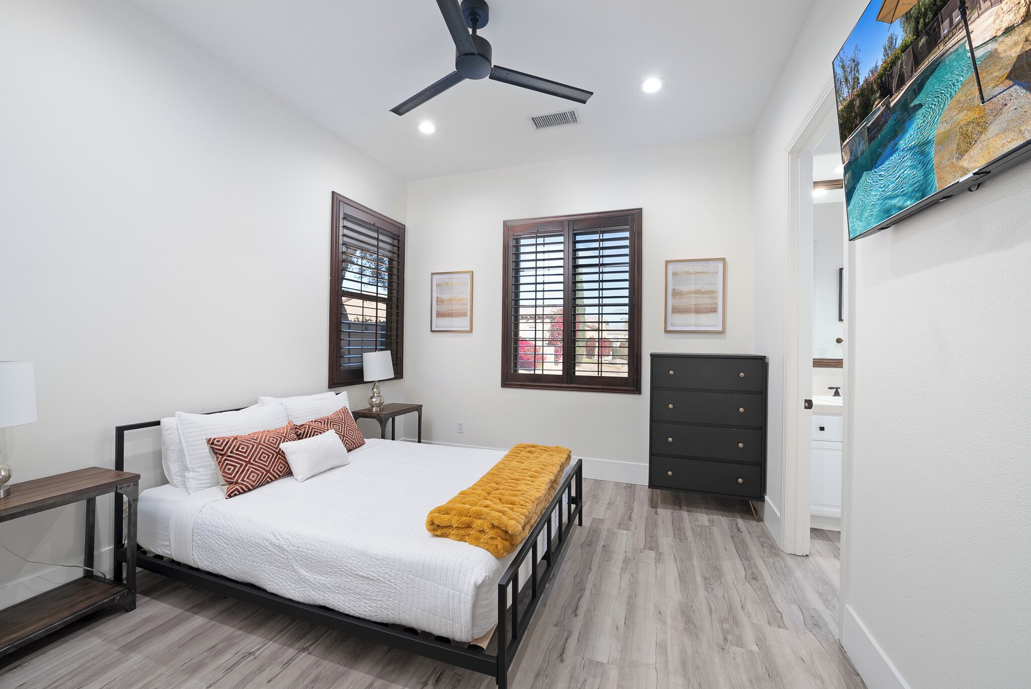 A bedroom with a bed, a ceiling fan, a TV, and a dresser.