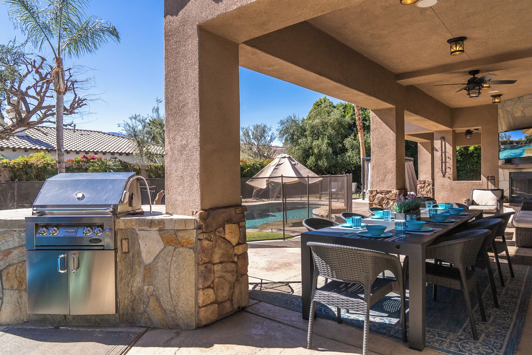An outdoor patio with a stone barbecue, a pool, and a dining area with chairs and tables.