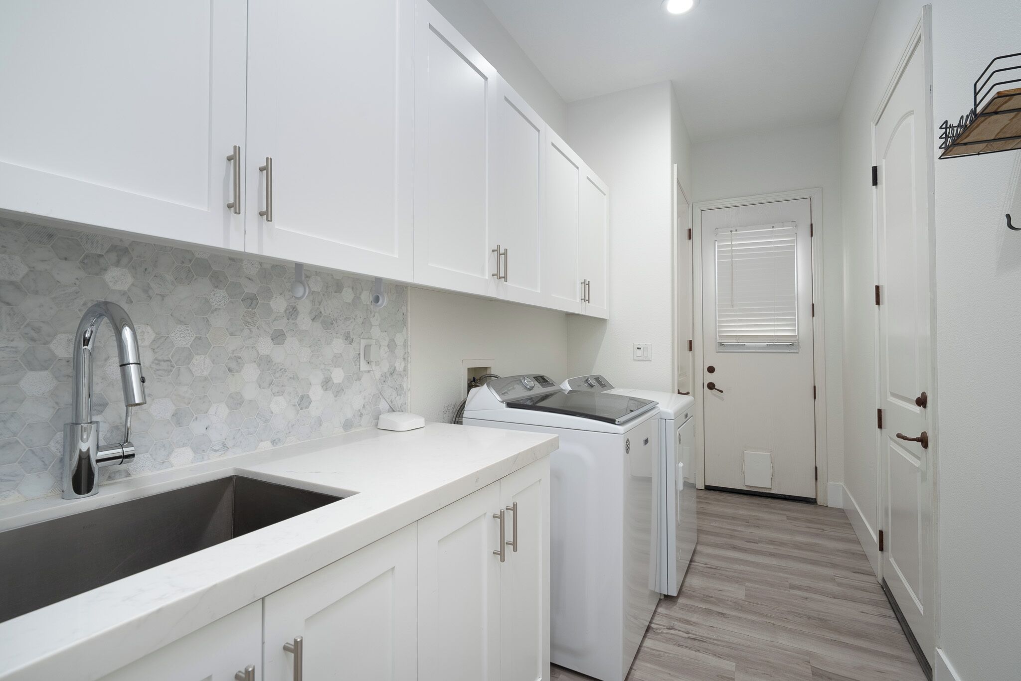 A modern kitchen with white cabinets, a stainless steel sink, and a washing machine.