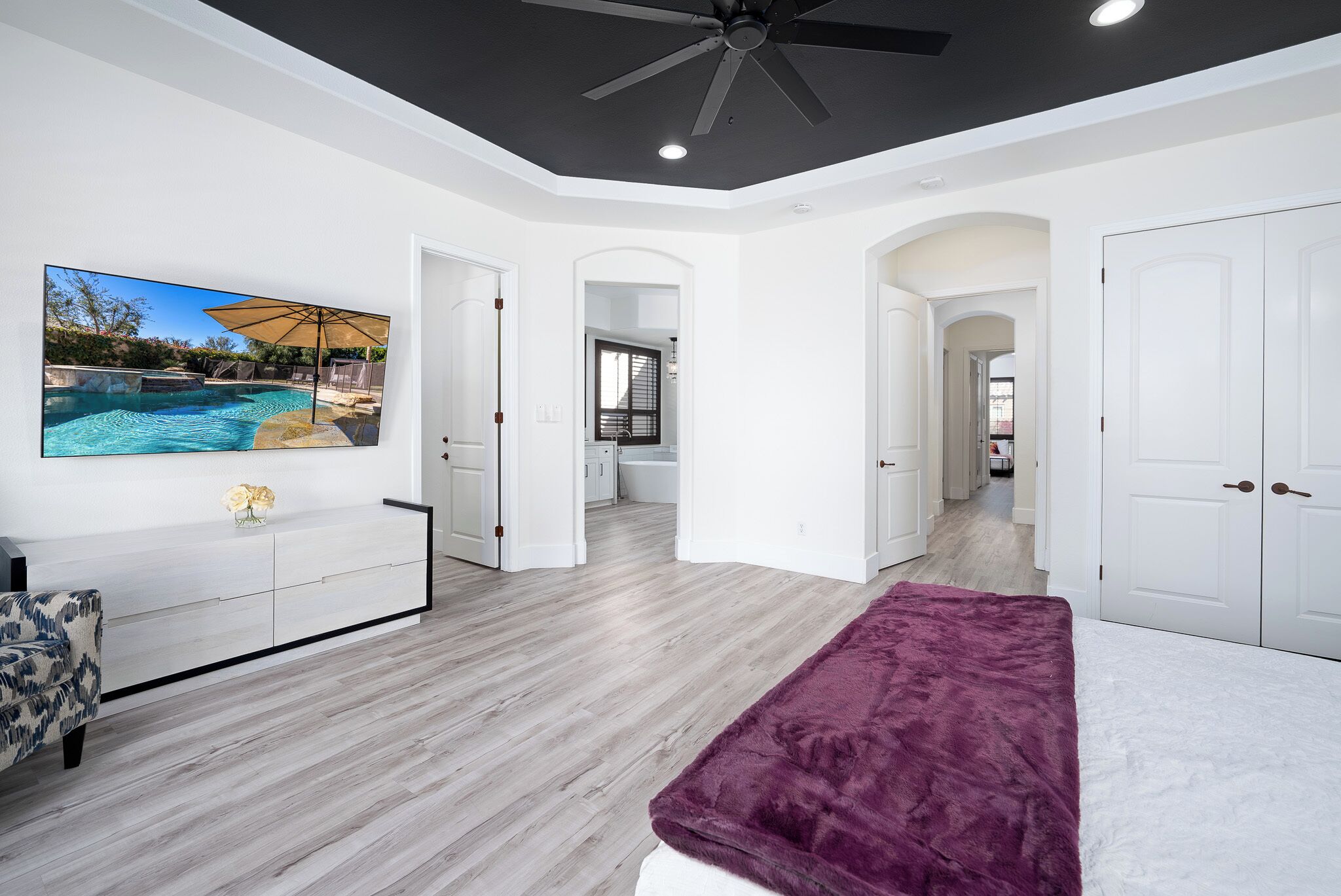 A modern bedroom with a large bed, a TV displaying a pool, and a hallway leading to a bathroom.