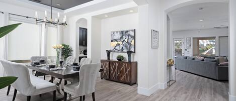 A modern dining area with a wooden table, white upholstered chairs, and a chandelier.