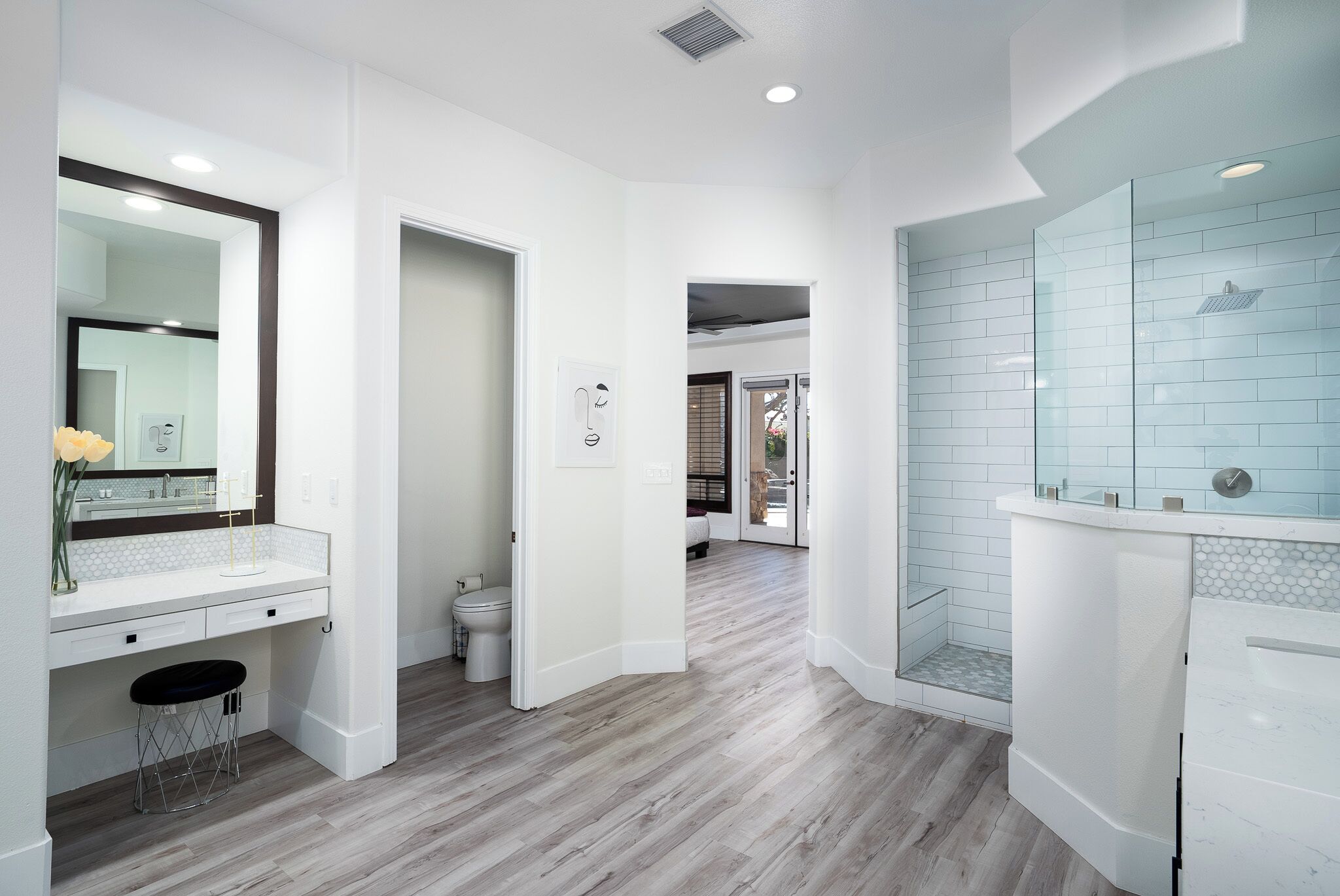 A modern bathroom with a white vanity, a glass shower enclosure, and a hallway leading to another room.