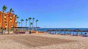 A beach with a hotel, palm trees, and beach umbrellas. - Vibe by the Sea of Cortez @Princesa Resort (Puerto Peñasco, Son)
