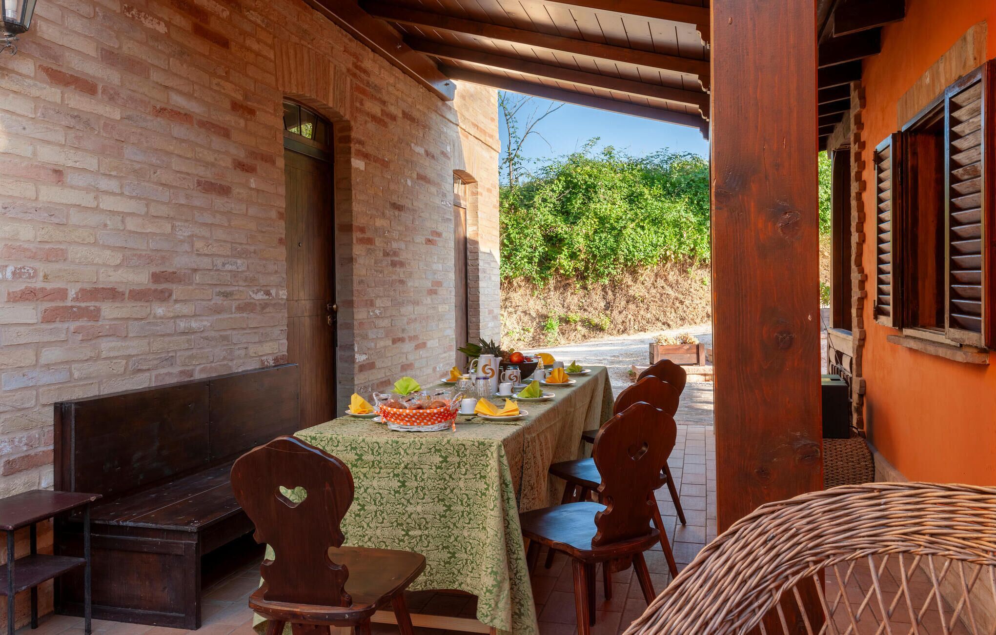 An outdoor dining area with a brick wall, wooden chairs, and a table set with plates, glasses, and a bowl of fruit.
