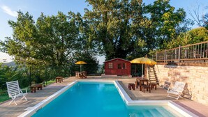 A swimming pool with a wooden deck, surrounded by trees and a small red building. - Lovely home in Morrovalle (Morrovalle)
