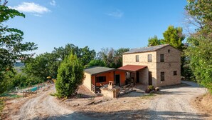 A two-story stone building with a small attached structure, a gravel driveway, and a pool area with lounge chairs. - Lovely home in Morrovalle (Morrovalle)