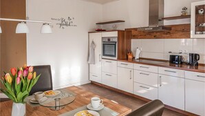 A modern kitchen with white cabinets, a wooden countertop, and a built-in oven. There is a vase with tulips on the dining table. - Nice home in Schneverdingen with WiFi (Schneverdingen)