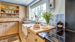 Een keuken met houten kastjes, een groot raam en een klok aan de muur.