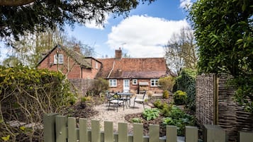 A brick house with a garden, a wooden gate labeled "The Bolthole," and a table and chairs in the yard.