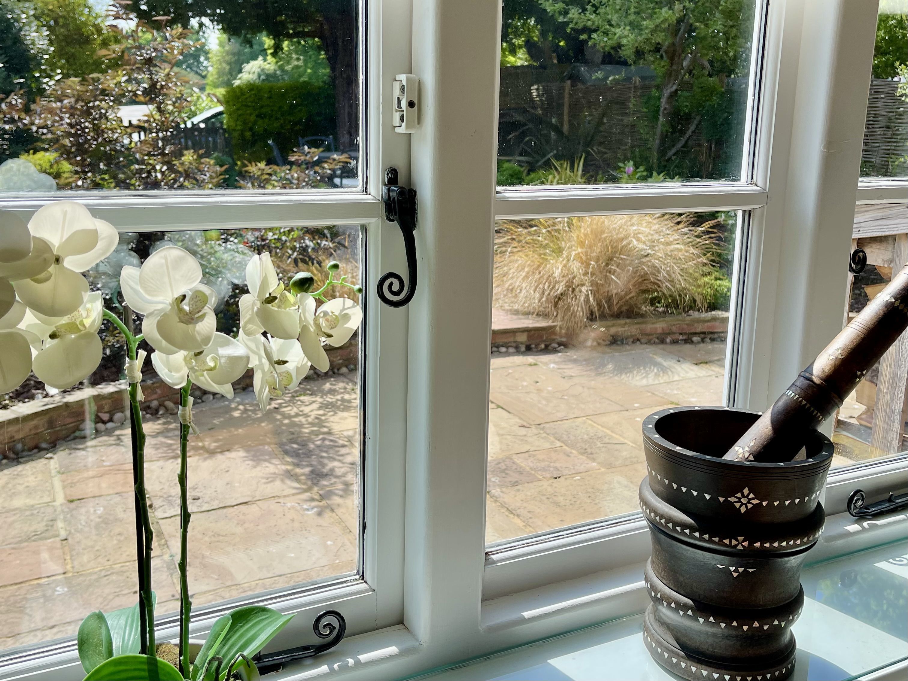 A window with a view of a garden, a potted orchid, and a decorative metal pot.