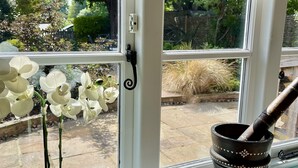 Een raam met uitzicht op een tuin, een potorkidee en een decoratieve metalen pot.