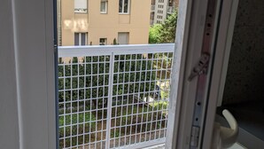 Udsigt fra en balkon med gelænder, der viser et brobelagt område og en bygning med mange vinduer og balkoner.