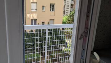 Vista da un balcone con ringhiera in metallo, su un’area lastricata di mattoni e un edificio con numerose finestre e balconi.