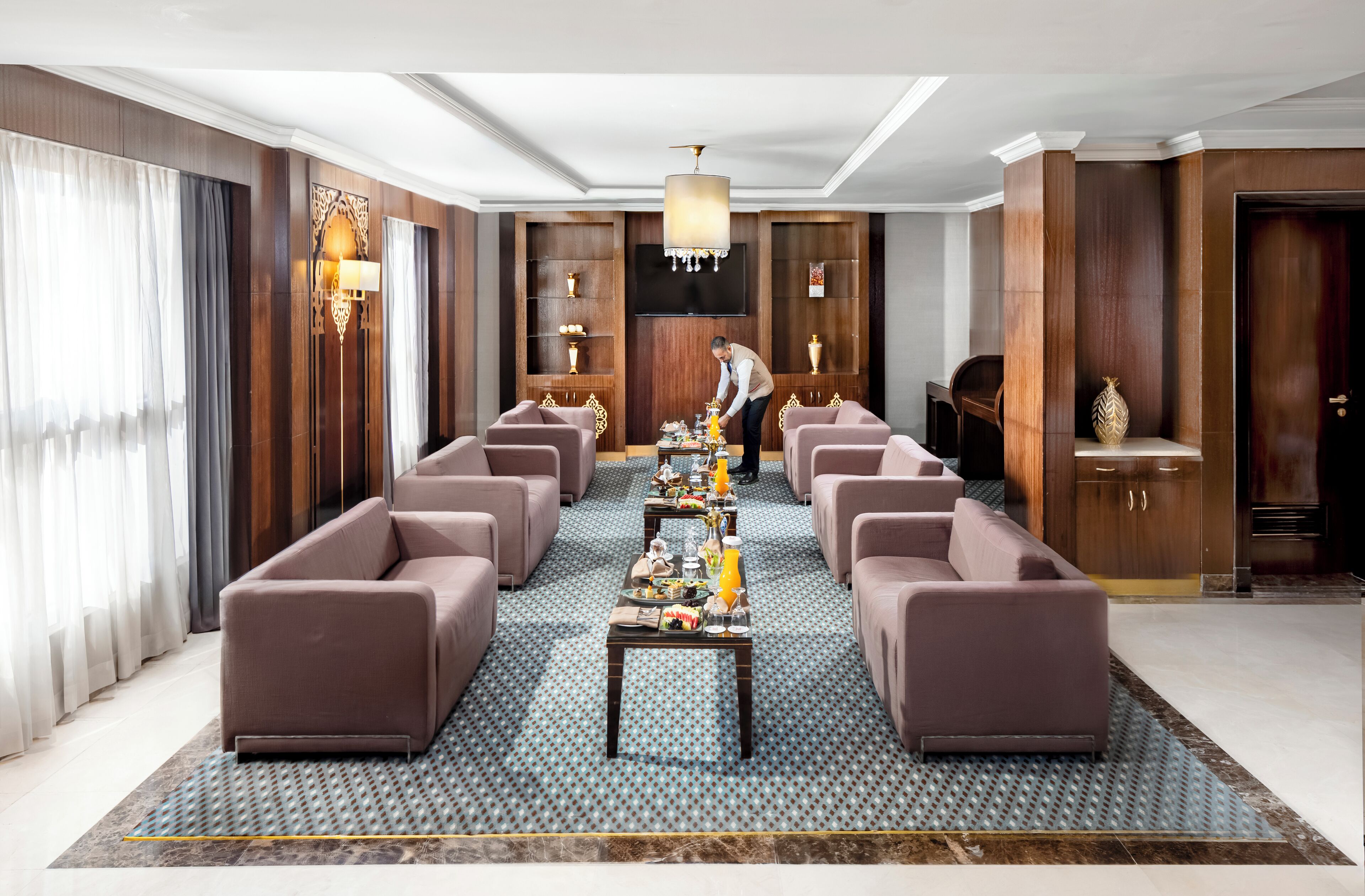A spacious hotel lobby with a long reception table, multiple sofas, and a chandelier.
