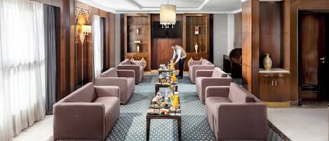 A spacious hotel lobby with a long reception table, multiple sofas, and a chandelier.