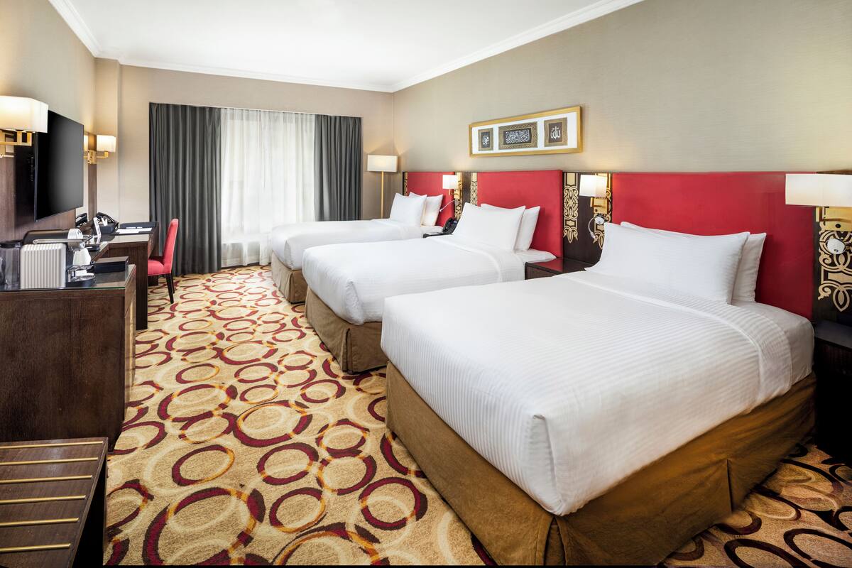 Une chambre d’hôtel avec trois lits, un bureau et une télévision.