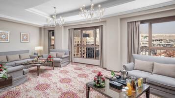 A spacious living room with a large window offering a city view, a chandelier, and a patterned carpet.