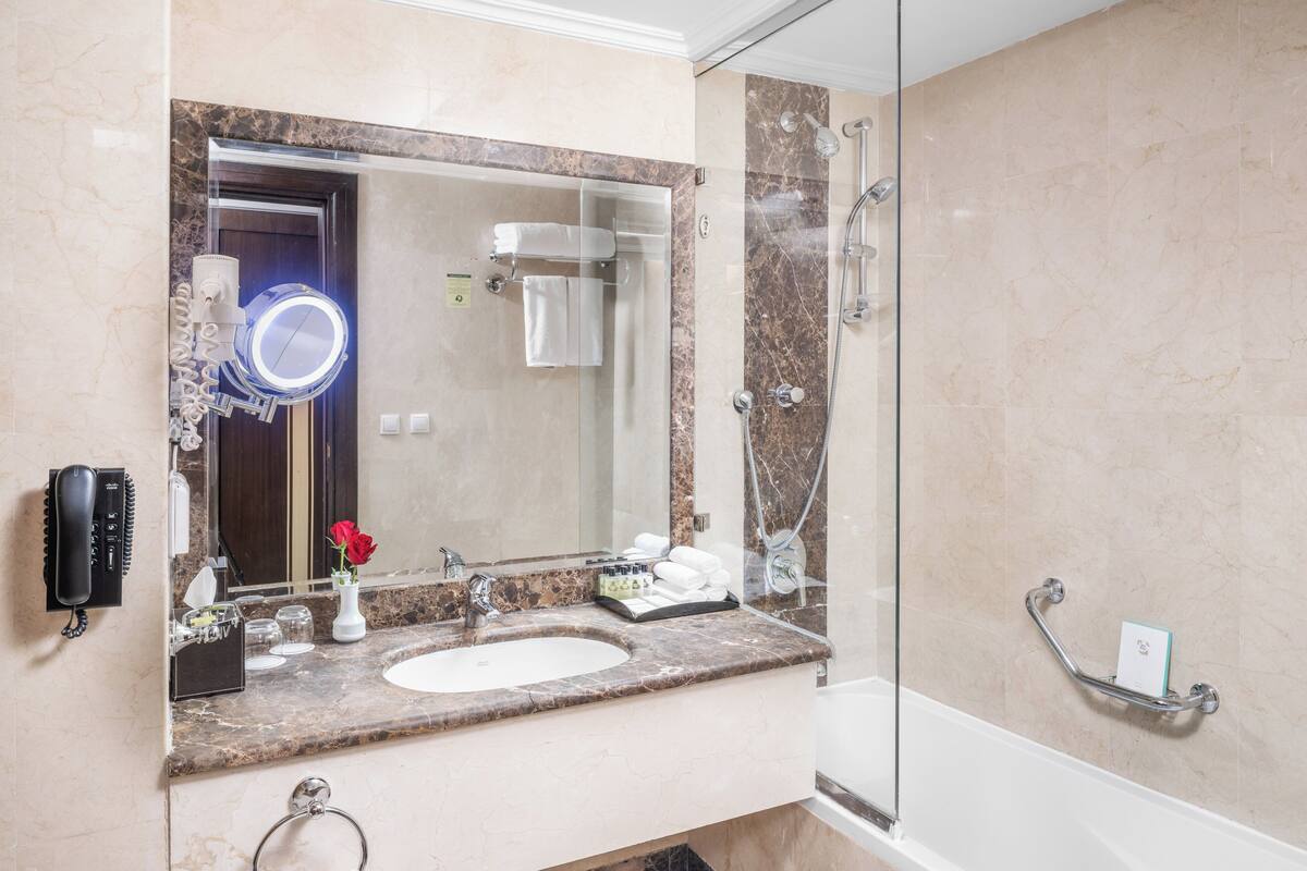 Une salle de bain avec un lavabo en marbre, un grand miroir, une douchette à main et un porte-serviettes.