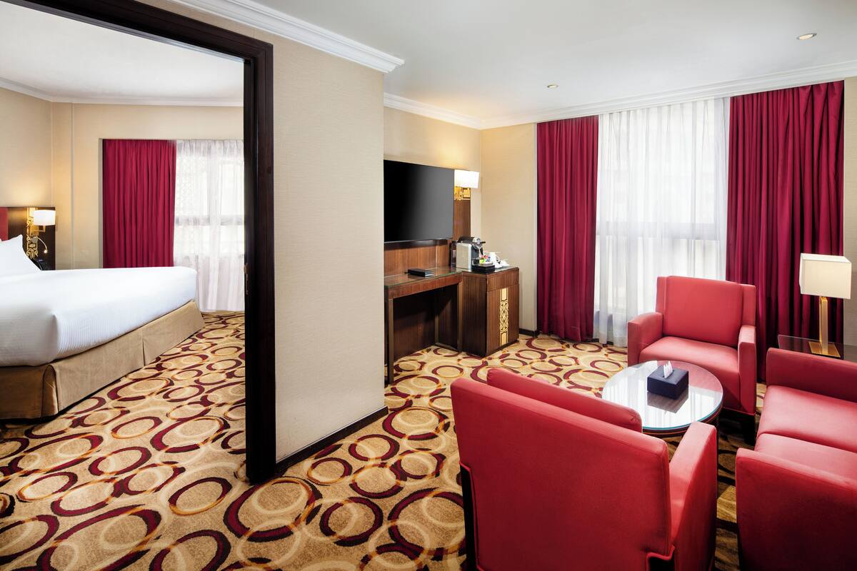 Une chambre d’hôtel avec un lit, un bureau, une télévision, une machine à café et des chaises rouges.