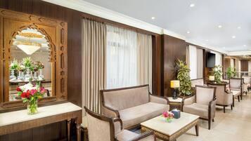 Eine Hotelhalle mit einer Couch, Sesseln, einem Couchtisch, einem Spiegel und einer Blumenkomposition.